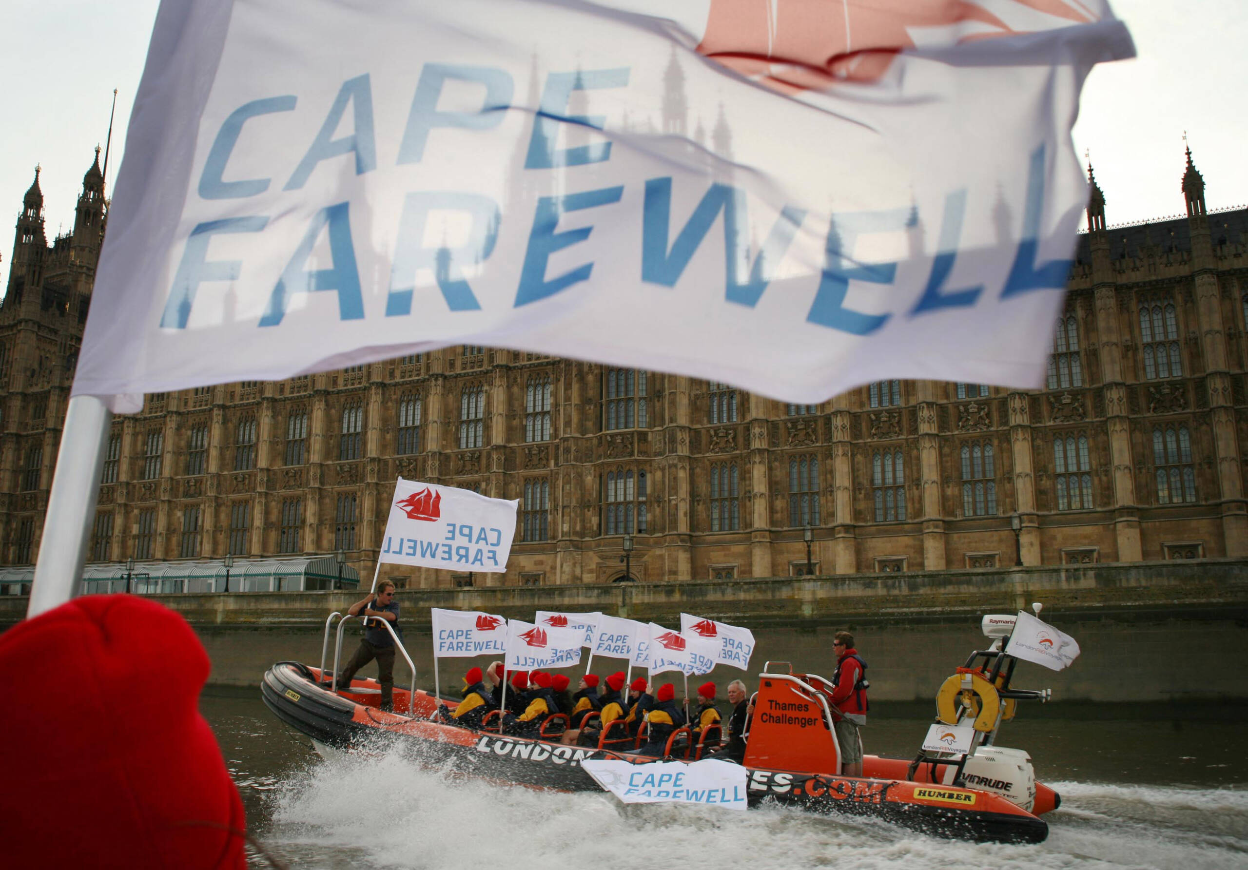 Photo of children on rib boat on River Thames in front of Houses of Parliament, Cape Farewell flag flying.